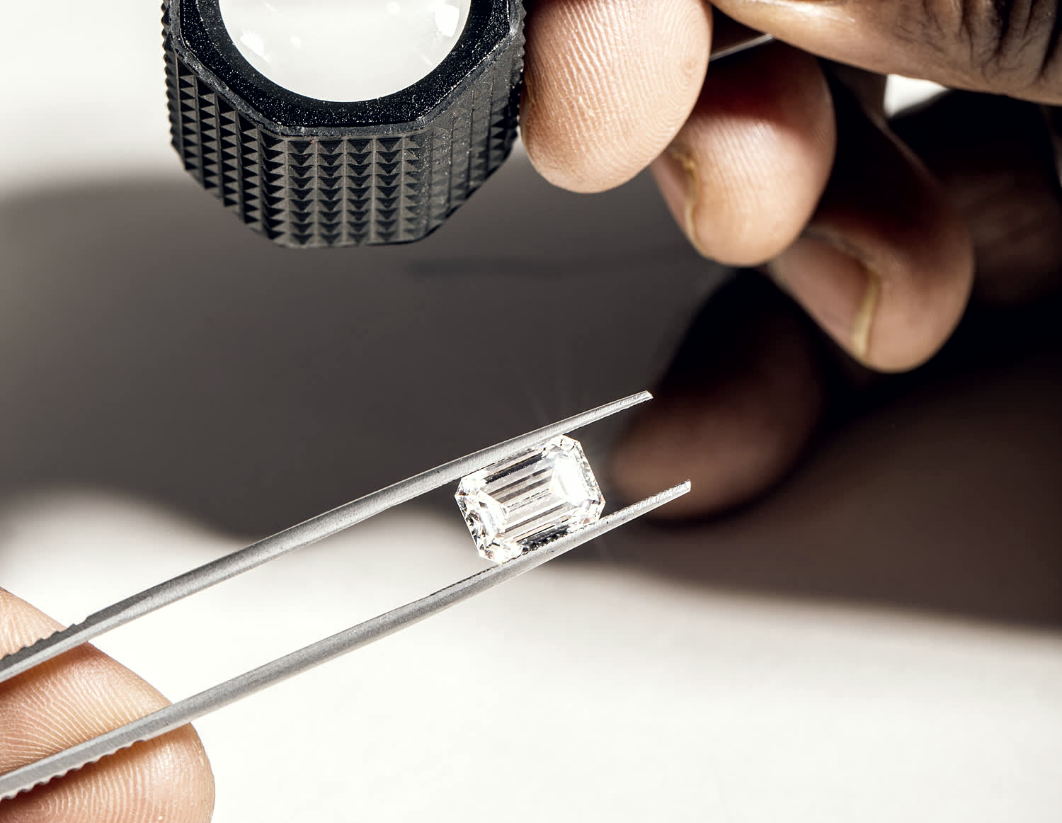 A finished emerald cut stone held in tweezers beneath the KIRA loupe